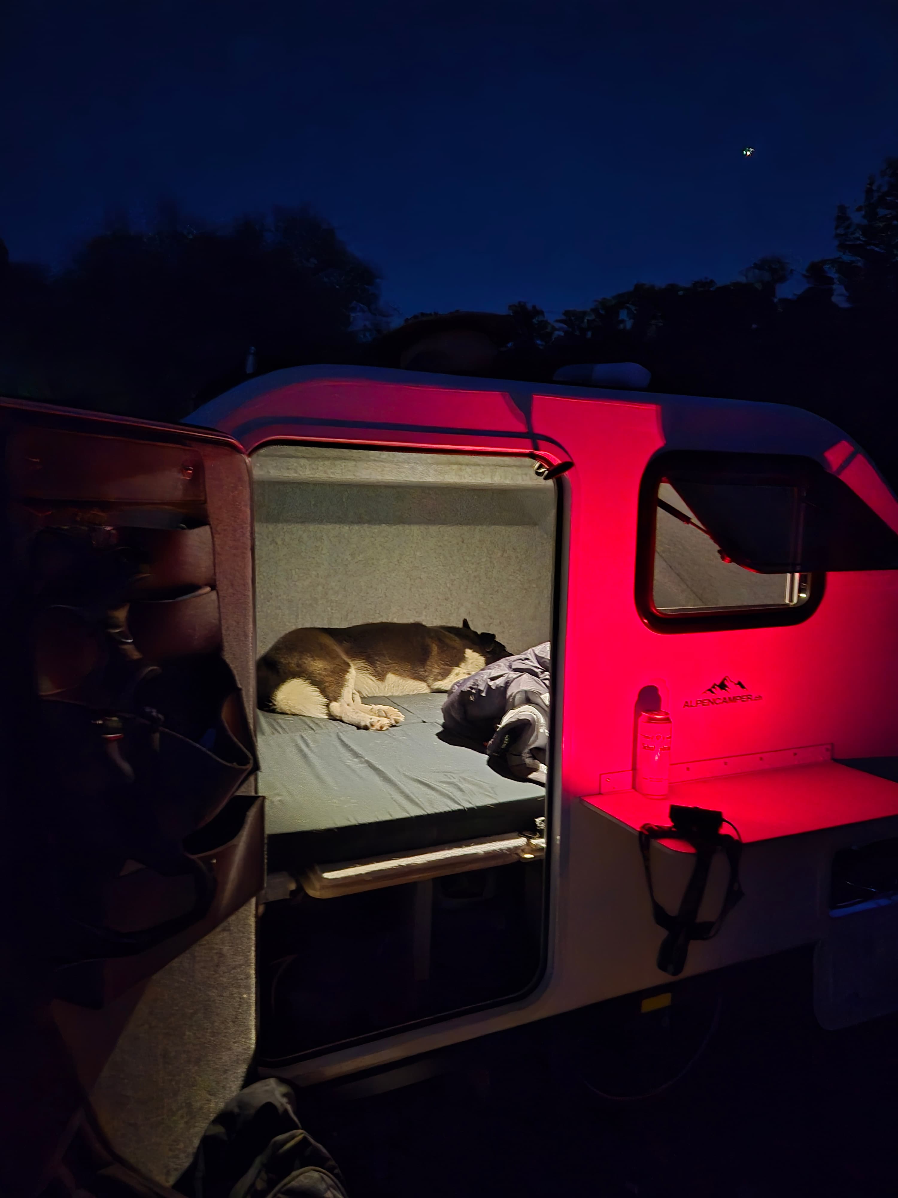 Nachtlager: Der Camper leuchtet rot in der Dämmerung, drinnen schläft Alex schon auf dem Bett